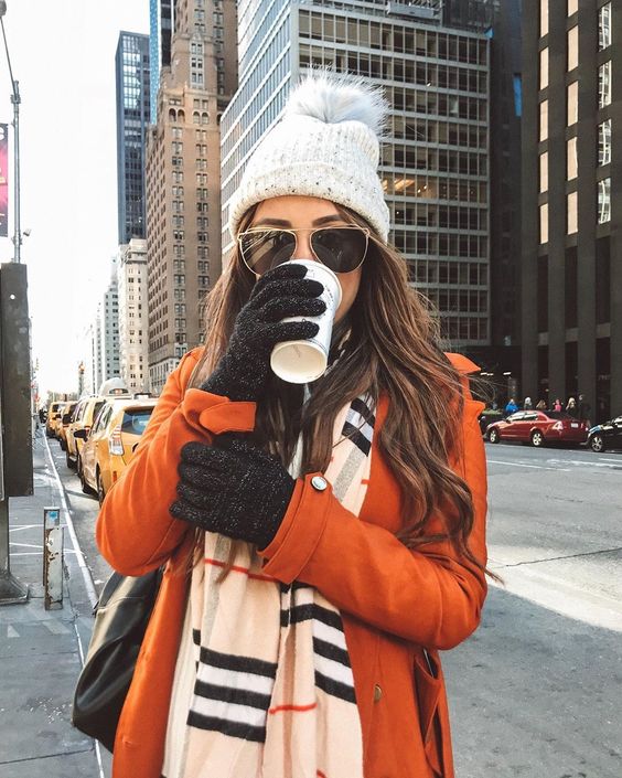 woman with orange coat drinking coffee with warm gloves